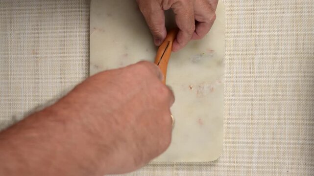 A sausage is being cut lengthwise with a kitchen knife on a white cutting board. Two hands hold the sausage and knife.