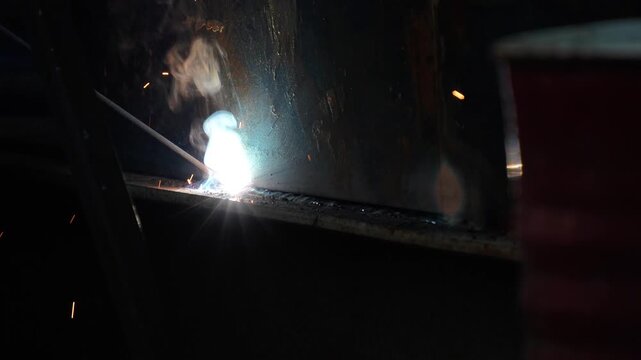 Close up of industrial arc welding with bright sparks, flash, and smoke
