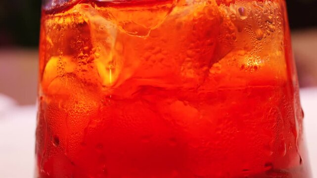 Macro shot of cold negroni cocktail with ice cubes and condensation on glass surface.