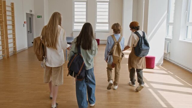 Rear view of diverse teenagers with backpacks walking through school recreation room past ping pong table. Footage is ideal for high school enrollment promos and educational marketing campaigns