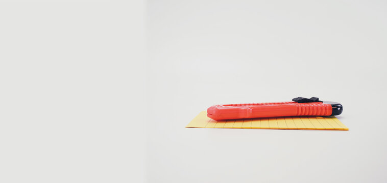 Taglierino in plastica di colore arancio e fogli di carta gialla per appunti su una superficie bianca e vuota con spazio testo