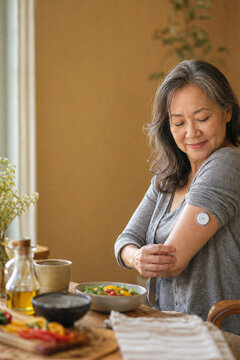 East Asian senior woman checking a continuous glucose monitor in the kitchen