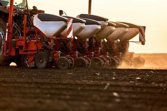 Tractor seeding spring crops in agricultural field creating dust at sunset