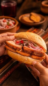 Hands holding a Peruvian pan con chicharron sandwich
