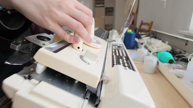 Person operating modern flatbed knitting machine to create professional textile garments in studio.