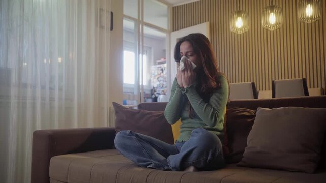 Sick young woman blowing nose in home for allergy, virus and sinusitis cold. Sneeze, flu and allergies of female face on couch in recovery from healthcare problem, medical disease and hay fever