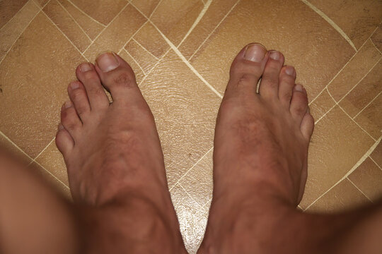 A top-down view of bare male feet on a tiled floor.