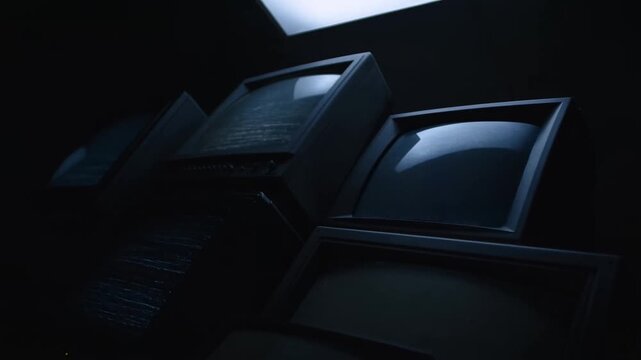 Slow motion tilt and pan across stacked crt television monitors showing static and flicker in dark interior studio room