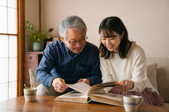 Japanese grandfather and adult granddaughter sharing a family photo album,家族のアルバムを一緒に見る日本人の祖父と成人した孫娘