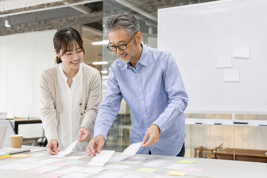 Young employee and senior mentor developing ideas with paper prototypes,紙のプロトタイプでアイデアを練る若手社員とベテランの指導者