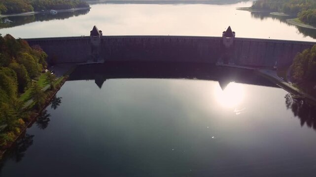 The M&ouml;hne Dam (M&ouml;hnetalsperre) is a masonry dam located in North Rhine-Westphalia, Germany. Aerial view dolly out. It is famous for the air raid by the British "Dambusters" during World War II.