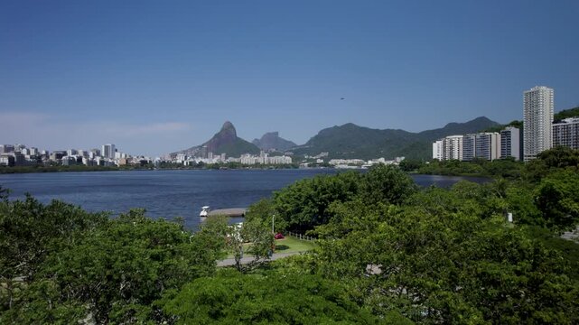 Drone going up behind a tree and revealing the Rodrigo de Freitas laggon in a sunny beatiful day. Rio de Janeiro,Brazil.