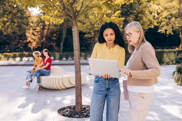 Naklejka premium Beautiful senior and young African American women using laptop working on the street outdoors