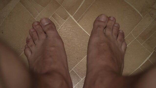 A top-down view of bare male feet on a tiled floor.