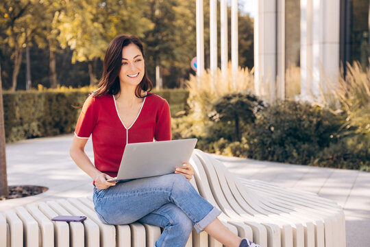 Confident smiling woman holding laptop, freelancer working, sitting on bench in university campus