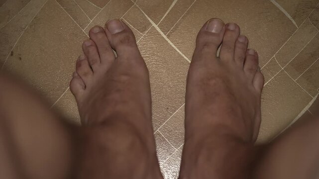 A top-down view of bare male feet on a tiled floor.