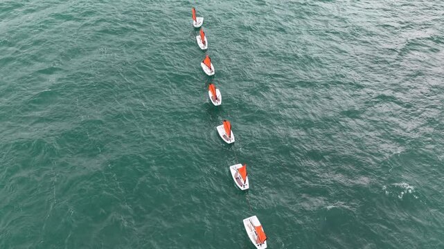 Overhead drone aerial row of small sailing dingles with orange sails flapping