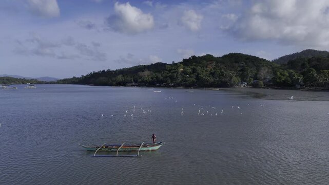 Aerial drone view of Fisherman carrying a container through shallow water beside a boat in Malampaya Sound