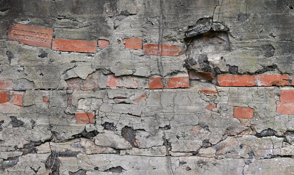 Decaying cement-rendered wall surface with cracked weathered parge, exposed broken red brick, dark underlayer, ridged cement render and dried vines across horizontal masonry surface