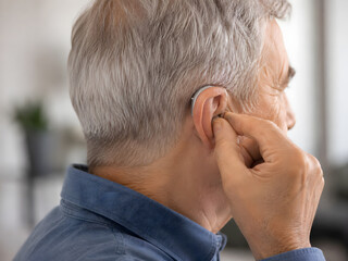 Fototapeta premium Audiologist fitting a modern hearing aid device onto a senior man's ear.