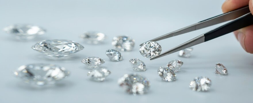 Hand holding diamonds with tweezers, sparkling gemstones collection on a light blue surface. Luxury jewelry concept for sale.