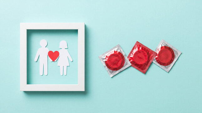 Safe sex and contraception concept featuring red condom packs and a paper cut-out couple frame on a blue background. Ideal for health awareness and family planning.
