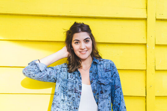 Portrait of smiling young woman in front of yellow wooden wall