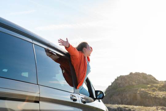 Happy woman leaning out of car window on a road trip