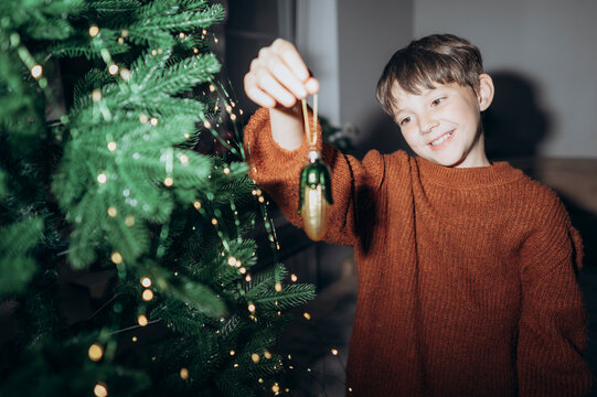 Happy boy hangs an ornament on the Christmas tree at home