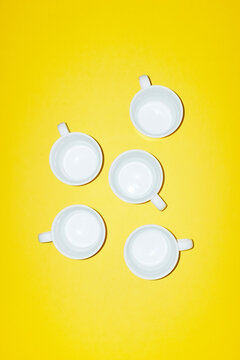 Five white empty coffee cups lie on a bright yellow background