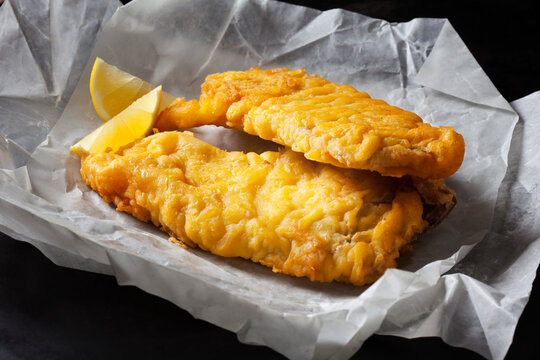 Fried coalfish filet and lemon slices on greaseproof paper