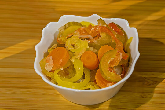 Cut pickled vegetables pile in ceramic bowl on table interior