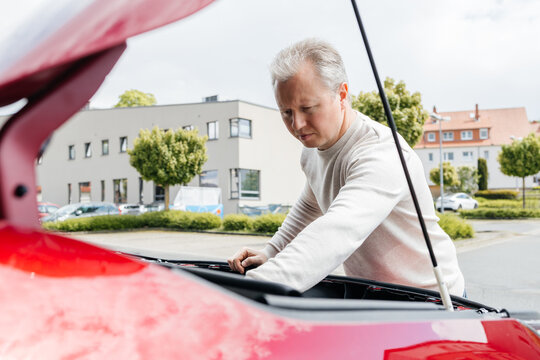 Car owner checking engine oil under the open hood outdoor