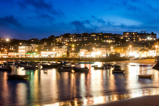 Small boats float in the illuminated harbor of St Ives at night