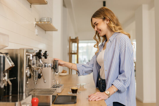 Happy woman makes morning coffee with a machine in the kitchen