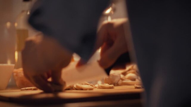 In a professional kitchen, a chef slices fresh champignon mushrooms on a cutting board with a white ceramic knife, preparing ingredients for a culinary dish with precise, careful technique