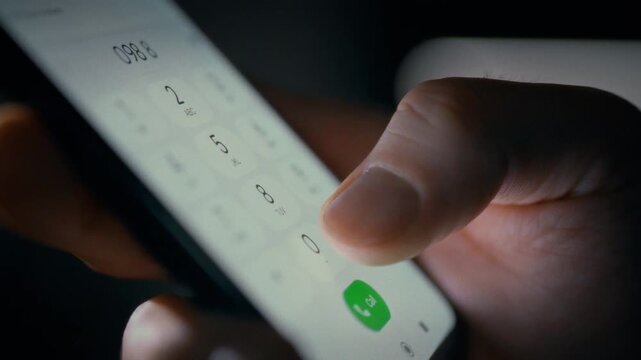 In an office, a man's hands clutch a sleek smartphone, his fingertips sliding across the touch keyboard to dial a number. The scene underscores everyday technology use and instant digital connection