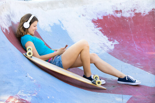 Female longboarder with earphones lying in halfpipe