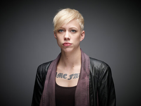 Portrait of blond young woman with tatoo in front of grey background