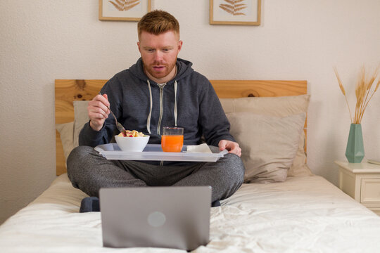 Man having breakfast in bed while using laptop in the morning