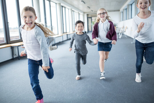 A group of enthusiastic schoolgirls hurrying through the hallway of their school with excitement and energy