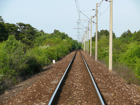 Railway tracks run through a lush green landscape under a bright blue sky.