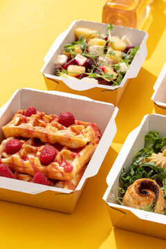 Healthy food meal boxes with sweet Belgian waffles raspberries beetroot pineapple salad and fish rolls on yellow background