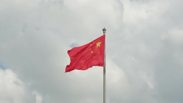 The national flag of the People's Republic of China flutters in the wind against a cloudy sky.