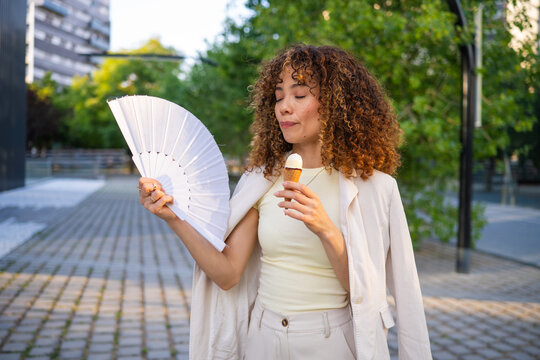 Young woman cooling down with fan and ice cream