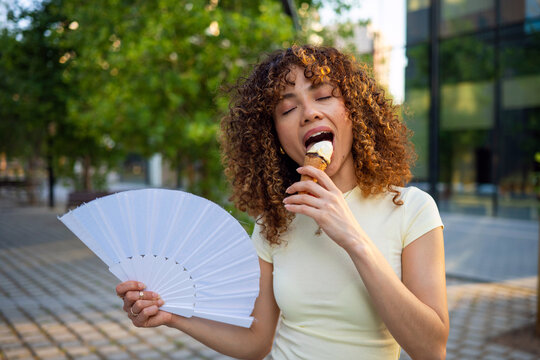 Woman enjoying ice cream and hand fan on hot summer day