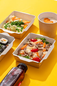 Healthy balanced food delivery ration with beef rice pilaf casserole mashed potatoes porridge sushi rolls and berry drink on yellow background