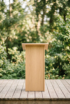 Minimal flat wooden podium for product presentation, outdoor stage, blurred natural greenery on background, clean elegant commercial composition. Mock-up. Close-up.