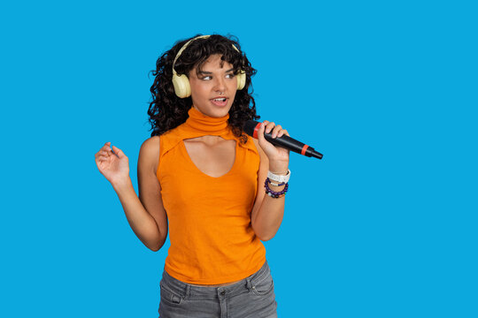 Young woman singing wearing headphones holding microphone