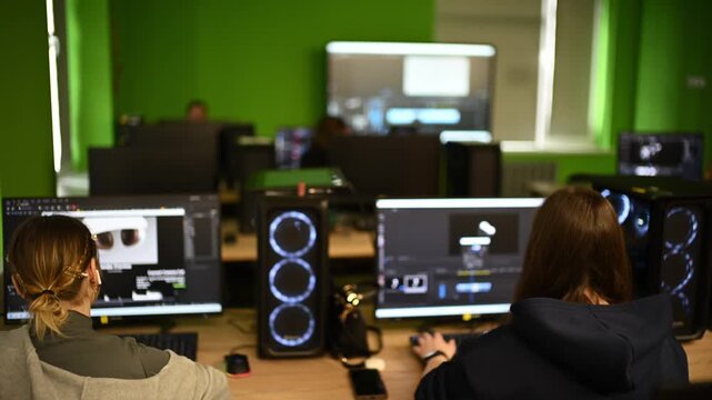 Young video editors working in professional production studio with green walls and powerful hardware.